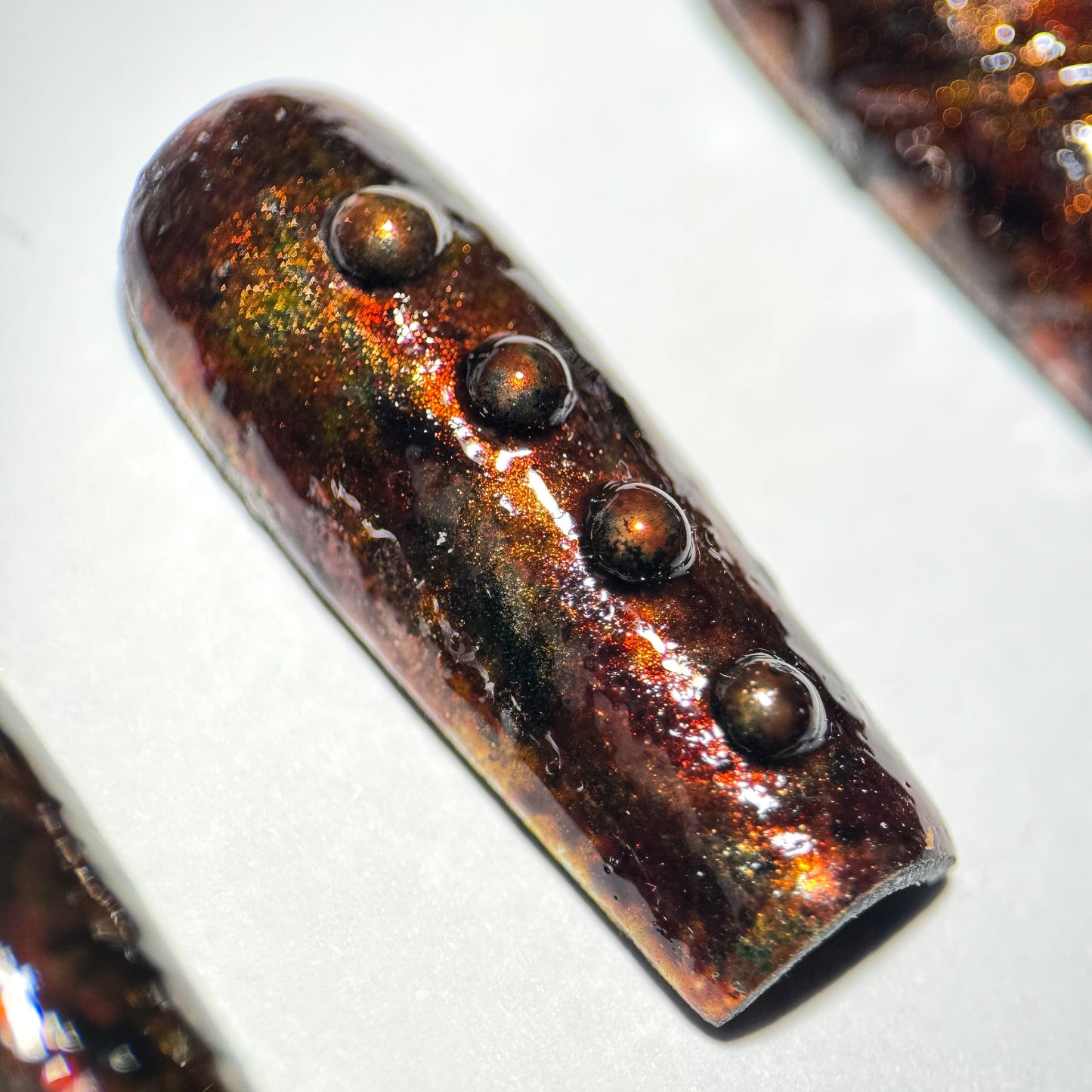 Press-on nail with a rusted metallic sheen and embedded stones on a white background