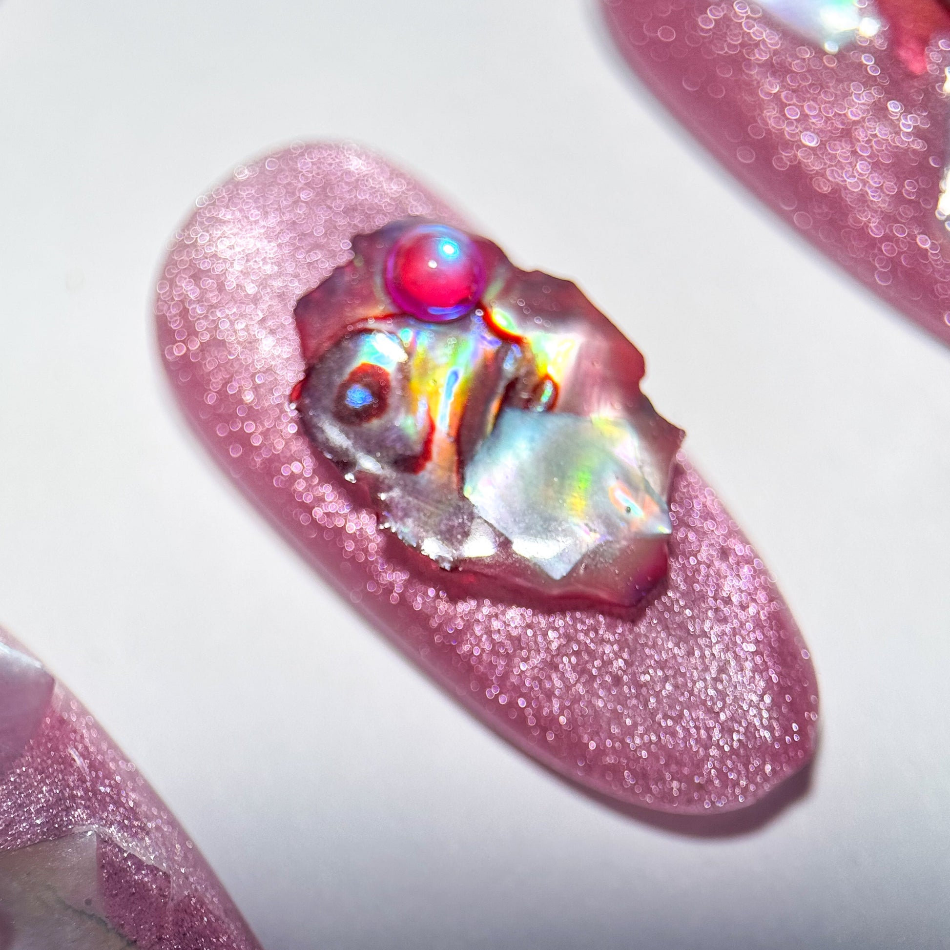 Pink glittery press-on nail with a colorful gem on a white background