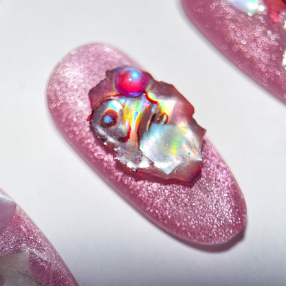 Pink glittery press-on nail with a colorful gem on a white background