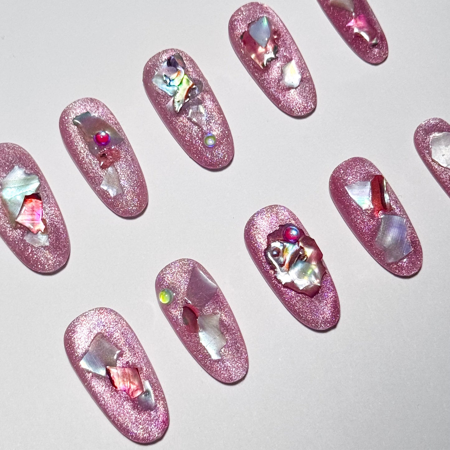 Pink glittery nail art with rhinestones on a light gray background