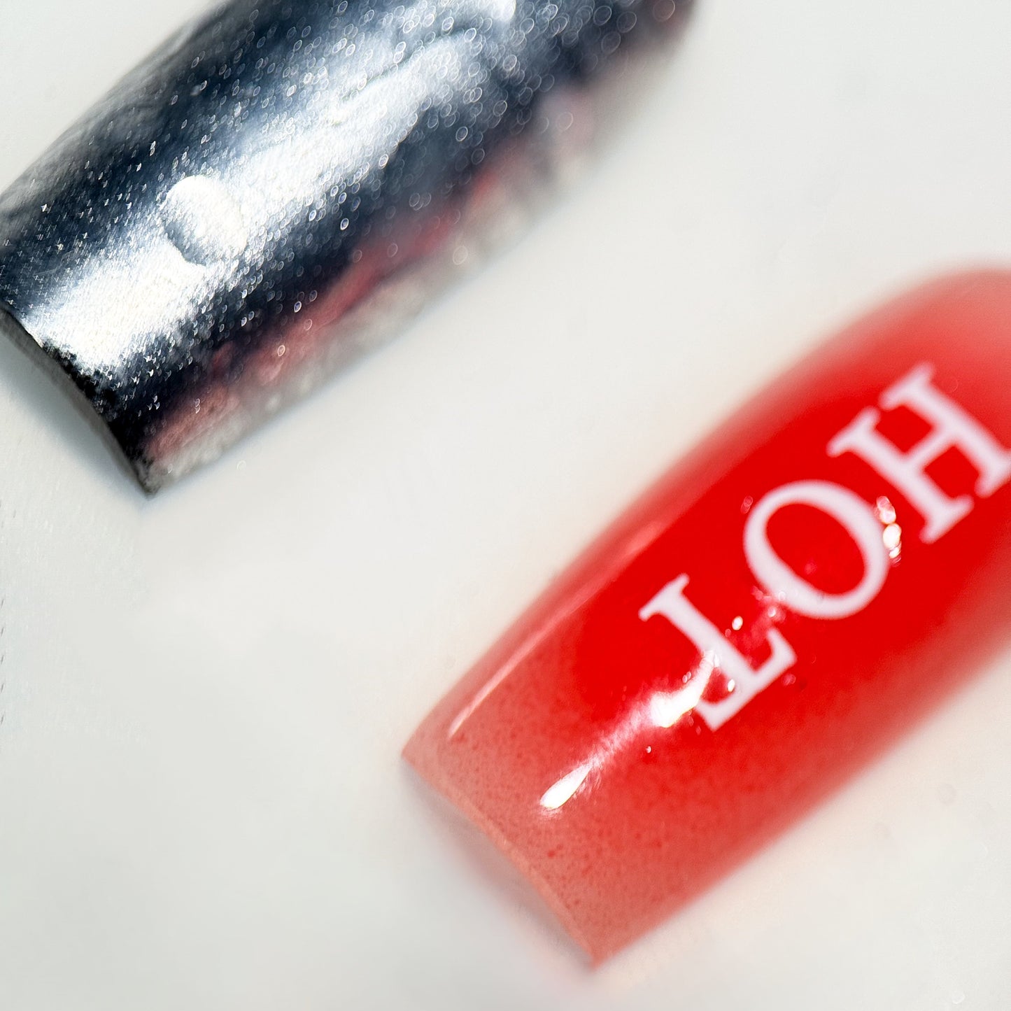Close-up of a red press-on nail with 'HOT' text on a white background