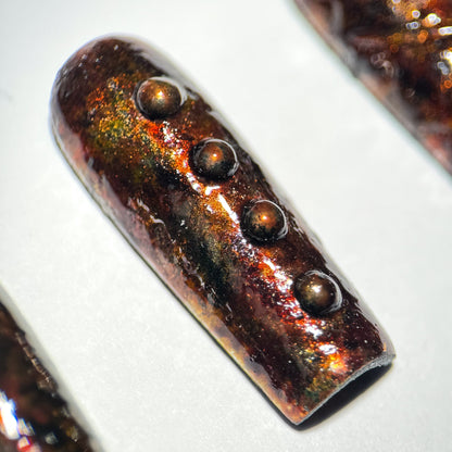 Press-on nail with a rusted metallic sheen and embedded stones on a white background